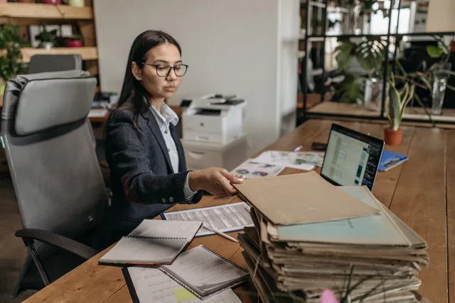 Businesswoman working at a wooden desk with documents and laptop in a modern office. Benchmarking accounting services before you appoint: scope and sources