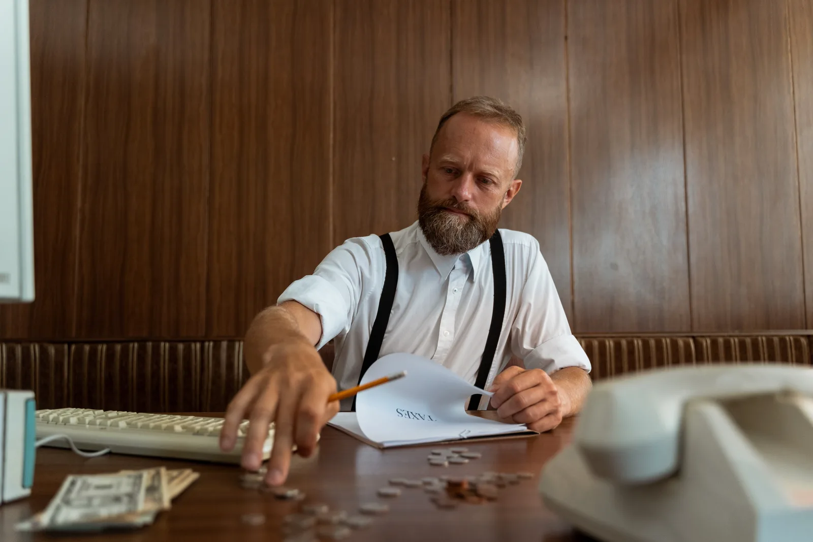 Bearded man in vintage office calculating finances with retro telephone and typewriter.