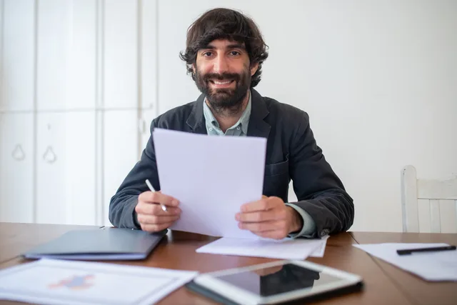 Smiling businessman in a black jacket reviewing documents at his desk, indoors. How to run an accounting services launch review