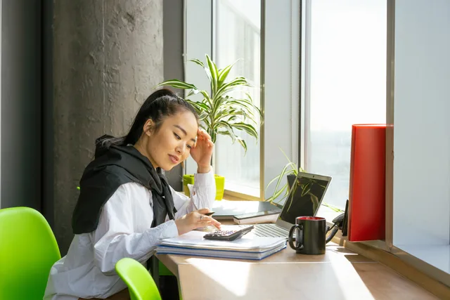 Asian woman working on finances with a calculator in a bright modern office. How to migrate an accounting practice onto new software in reconciled rounds