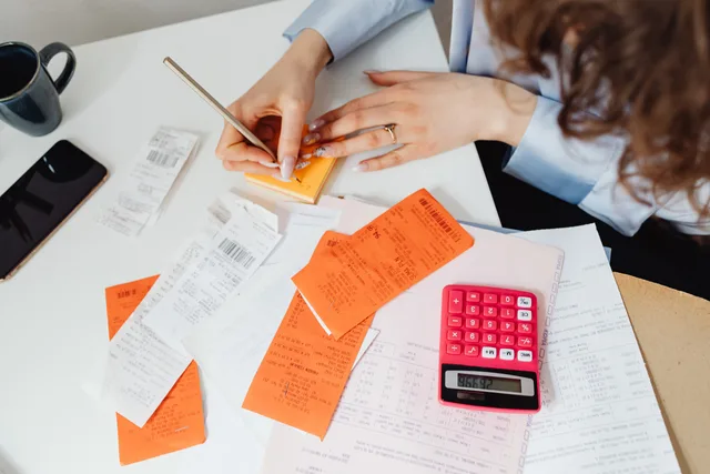 A woman writes down financial details using a calculator, receipts, and documents. How UK bookkeepers structure their fees