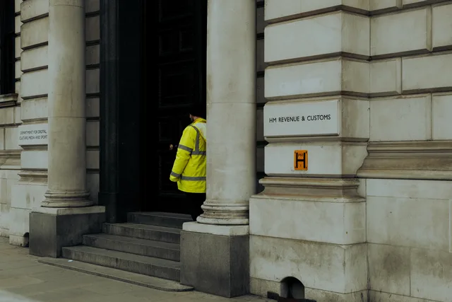 A guard in yellow jacket at the entrance of HM Revenue & Customs building in the UK. Cross-border VAT and payroll for UK and Irish accountants